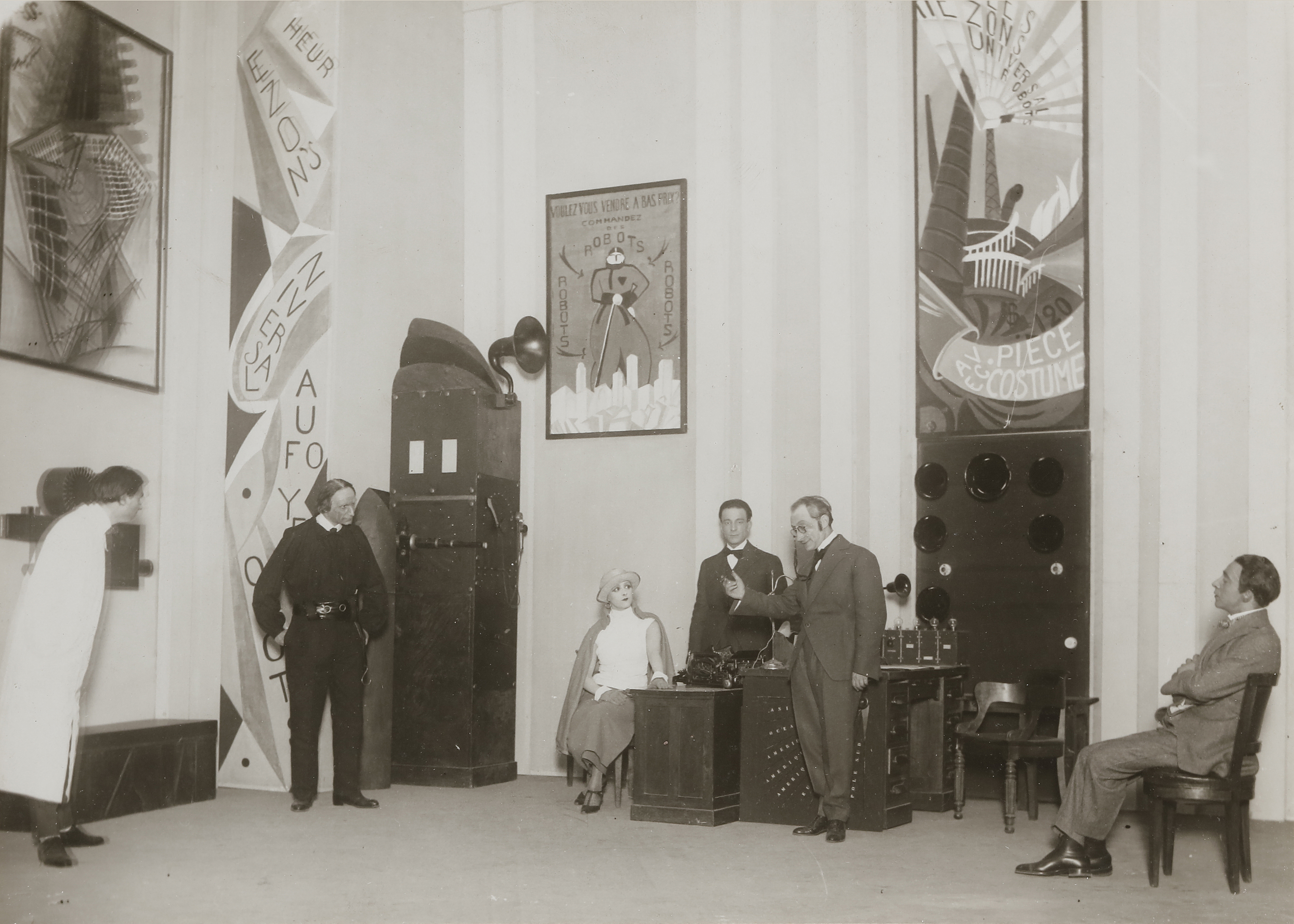 Scena z paryskiego przedstawienia R.U.R. w Comédie des Champs-Élysées, 26 marca 1924 r.; na ścianie plakat z napisem „Robots” (fot. Henri Manuel)